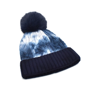 Detail of blue tie-dye knit winter beanie with large faux fur pom-pom and ribbed cuff