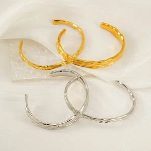 Dettaglio di bracciali rigidi testurizzati in oro 18K e argento su seta bianca