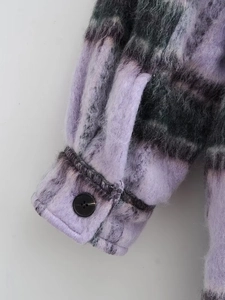 Close-up of plaid wool coat cuff featuring a black resin button and soft brushed texture