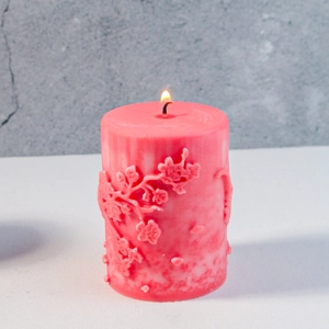 Nahaufnahme einer rosa Reliefkerze mit Blumenmuster und brennender Flamme