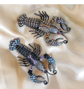 Detailed macro of two rhinestone lobster brooches on elegant champagne silk background
