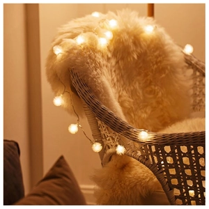 Detail of warm white LED pom-pom fairy lights on a cozy white faux fur rug