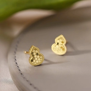 Detailed close-up of 18k gold plated gourd earrings with honeycomb texture on leather