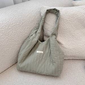 Detail of sage green ruched fabric texture and white label on minimalist shoulder tote bag