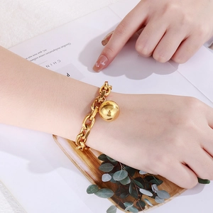 Close-up of gold hollow ball pendant on thick stainless steel chain bracelet on wrist
