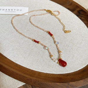 Detail of beaded necklace with 18k gold plating, pink beads, and red teardrop pendant