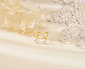 Close-up of golden twisted knot stud earrings with elegant white pearls on a soft background