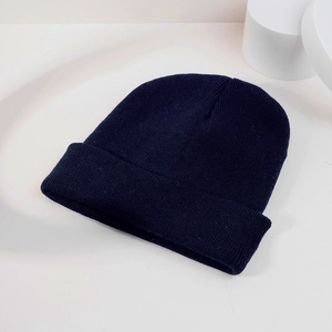 Close-up of dark blue ribbed knit beanie with folded cuff on a minimalist background