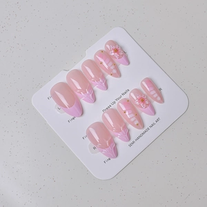 Detail of almond press-on nails with 3D embossed flowers and gold beads on pink French tips