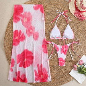 Flat lay detail of floral bikini set with mesh sarong on a woven mat with summer props