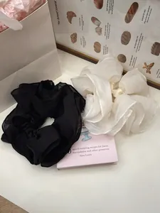 Detail of oversized ruffled mesh scrunchies in black and cream beige with airy texture