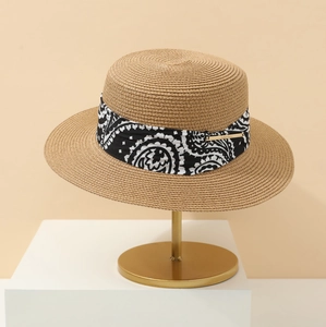 Close-up of a straw boater hat with paisley ribbon on a gold display stand