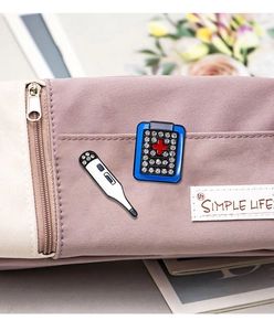 Detail of enamel thermometer and ambulance bag pins with rhinestones on a lilac pouch