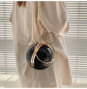 Dettaglio pochette a sfera in acrilico nero con manico ad anello oro e tracolla a catena