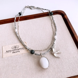 Détail d'un collier hirondelle vintage avec pierre blanche et perles sur bois