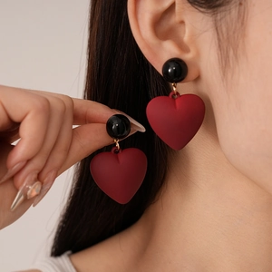 Close-up of a matte dark red heart pendant earring with a black bead stud on ear