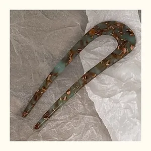 Detail view of U-shaped marble patterned acetate hair fork on minimalist white paper