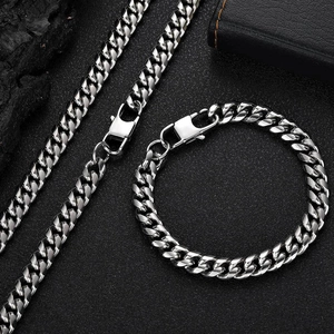 Silver stainless steel Cuban chain necklace and bracelet set on a black textured background
