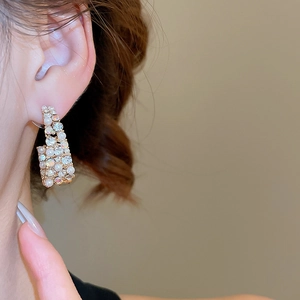 Detailed close-up of C-shaped earrings with inlaid pearls and sparkling crystals on model