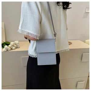 Close-up of a light gray PU leather crossbody bag worn by a model in a minimalist setting