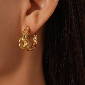 Détail d'une boucle d'oreille dorée en forme de C noué sur un modèle au fini métallique