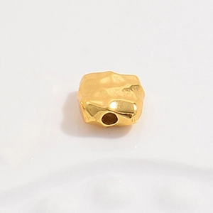 Macro shot of irregular square S925 silver bead with golden hammered texture and center hole