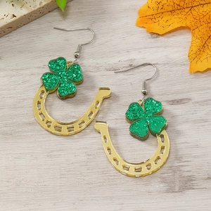 Golden horseshoe earrings with green glitter shamrock on light wood background
