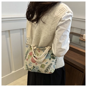 Close-up of a floral beige canvas tote bag worn cross-body in a cozy cafe setting