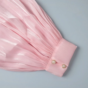 Detail of pink chiffon dress with pleated lantern sleeve and pearl button cuff detail