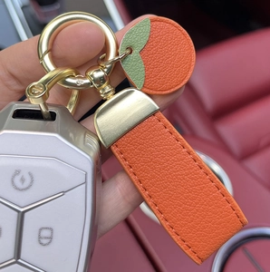 Detail of vibrant orange lychee leather car keychain with gold hardware on red interior