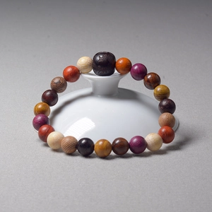 Multicolor wood bead prayer bracelet with carved beads displayed on white ceramic tea set