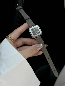 Dettaglio di un orologio quadrato dorato da donna con quadrante nero e cinturino grigio