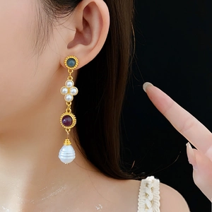 Close-up of vintage gold tassel earrings with colorful gems and irregular pearl on model