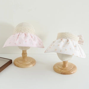 Detailed view of floral sun visors for girls with lace trim and bow on wooden stands
