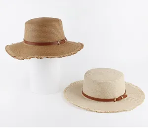 Flat top woven straw hats with leather belts and fringed edges in tan and cream colors