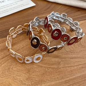 Three enamel elastic bracelets in gold, white, and red-orange on a wooden surface