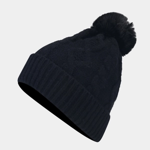 Detailed close-up of a black cable knit beanie featuring a large fluffy faux fur pom-pom