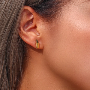 Detailed view of a gold coffee cup earring with green zircon accents on ear