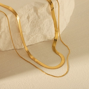 Detail of layered gold stainless steel snake chain and fine link necklace on rock
