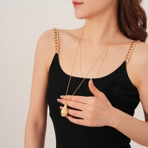Close-up of golden sweater necklace with frosted relief pendant on black knit top