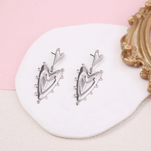 Macro shot of silver gothic heart drop earrings on a white vintage jewelry ceramic tray