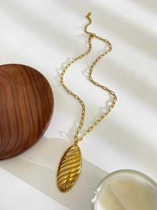 Macro detail of golden metal hollow oval pendant with striped texture on a chain