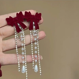 Détail de boucles d'oreilles nœud en velours rouge avec glands de perles et strass