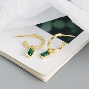 Close-up of gold bamboo-textured C-shape earrings with emerald green zircon pendants