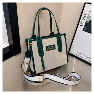 Detail view of canvas tote bag featuring green leather trim and wide white shoulder strap