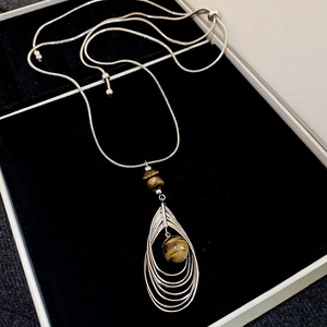 Detail of tiger eye stone pendant and layered metal teardrop frames on a snake chain necklace