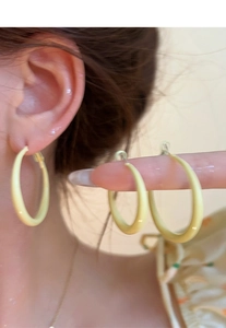 Close-up of matte cream yellow hoop earrings showing size scale and ear placement