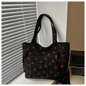Close-up of black corduroy tote bag featuring red strawberry print and zipper pocket