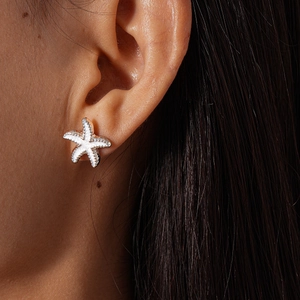 Close-up of a white starfish earring with gold trim worn by a model on the earlobe