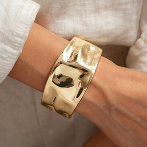 Detail of wide gold textured cuff bracelet featuring wavy hammered finish on model wrist